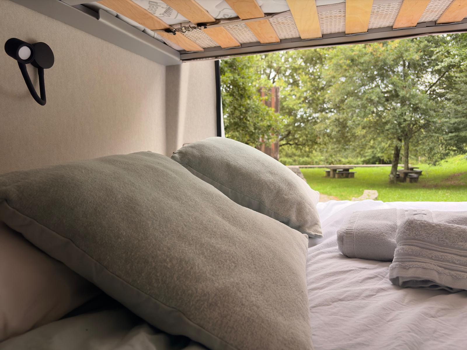 Cama de la camper con cojines y vistas al exterior verde